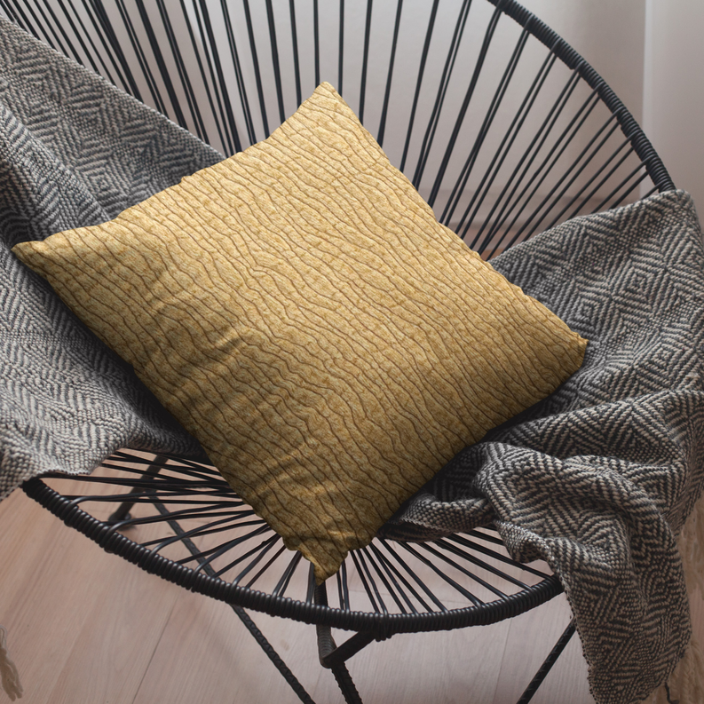 Yellow throw pillow with wavy desert-line textured fabric on a patterned blanket