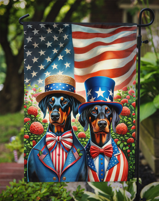 Patriotic Doberman garden flag hanging on stake with two dressed dogs