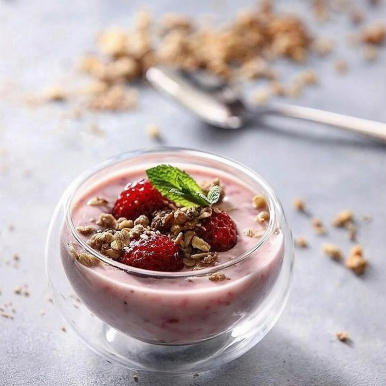 Transparent glass bowl with yogurt, strawberries, and granola, clear rim