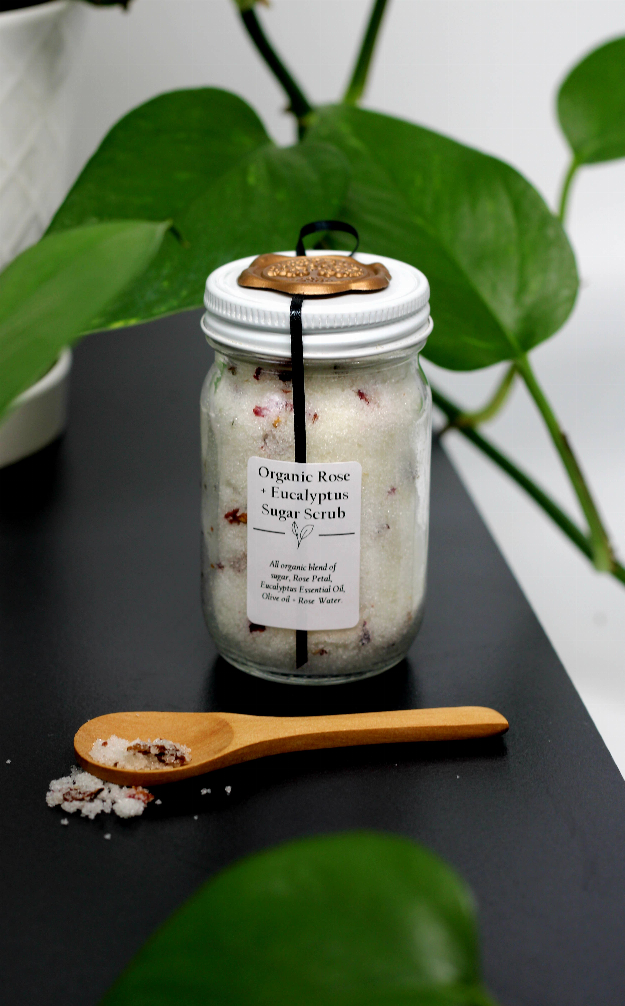 Sugar scrub jar with printed label and gold lid, wooden spoon on the surface