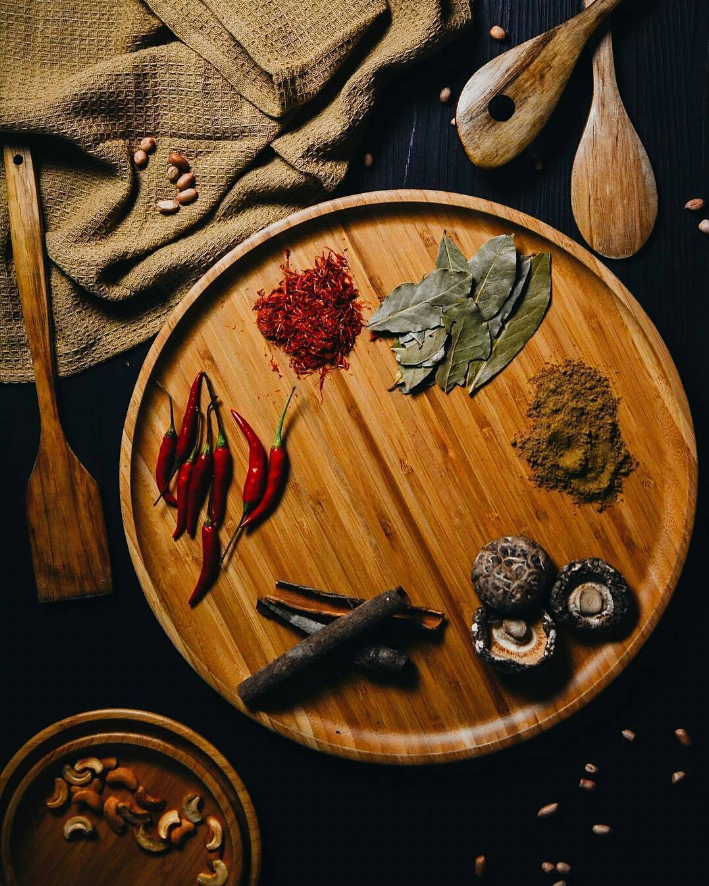 Round wooden serving plate with herbs and spices arranged on top