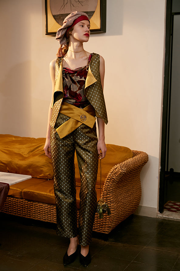 Corset-style yellow belt with gold logo buckle at waist over patterned pants