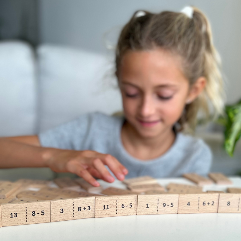 Wooden number domino tiles on a table while a child builds a domino layout