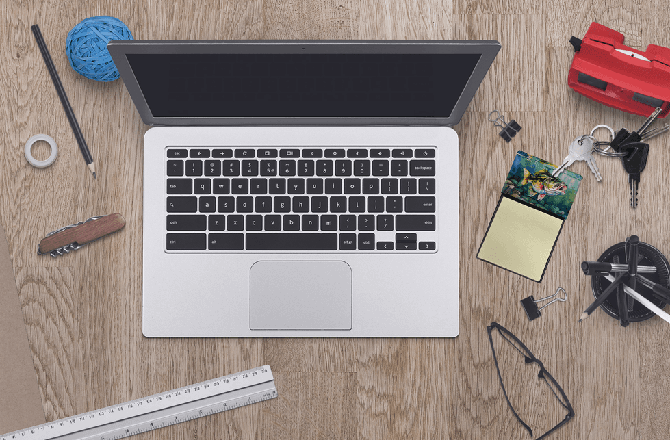 Silver laptop on a wooden desk surrounded by office supplies, including a blue yarn ball and stationery items.