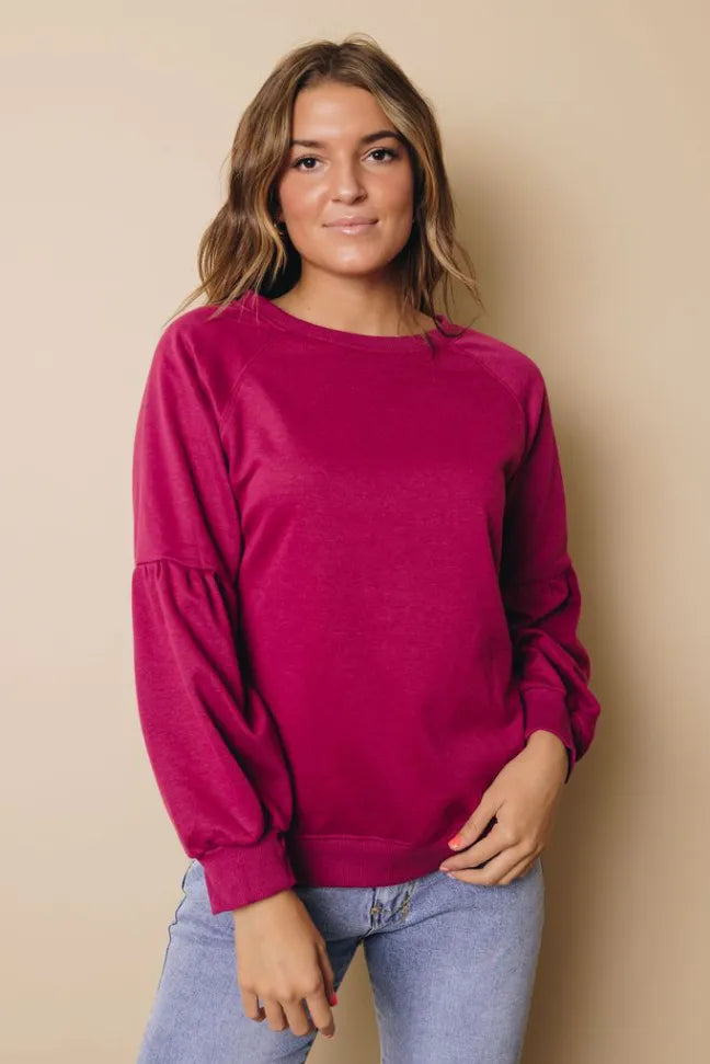Magenta balloon-sleeve sweatshirt with crew neck, front view with one hand on hip