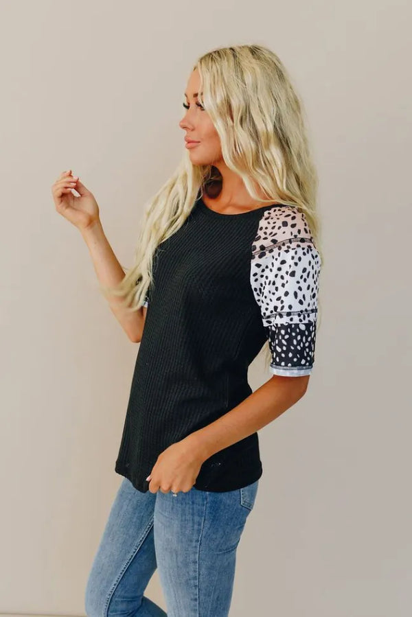 Black knit top with white spotted raglan sleeves and round neckline.