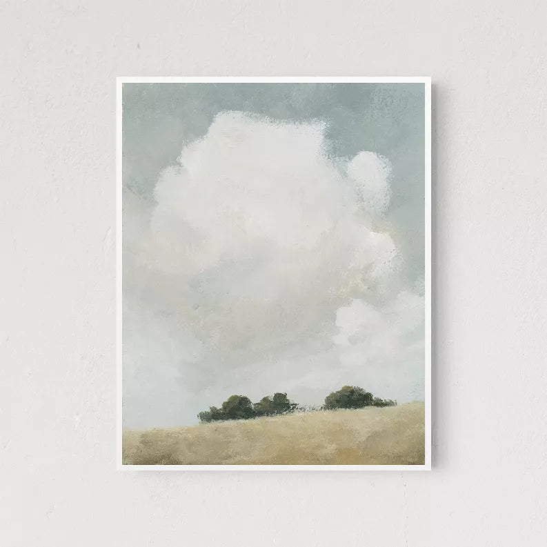 White bordered wall art print with cloudy sky, green trees, and beige hill