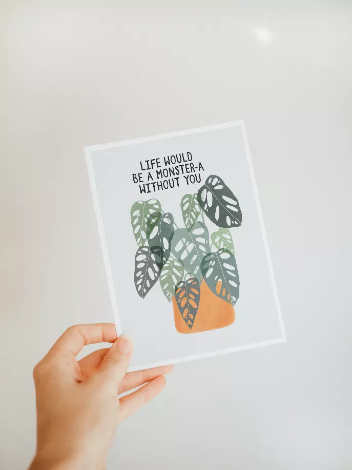 Hand holding framed monstera leaf wall art print with quote and white border.
