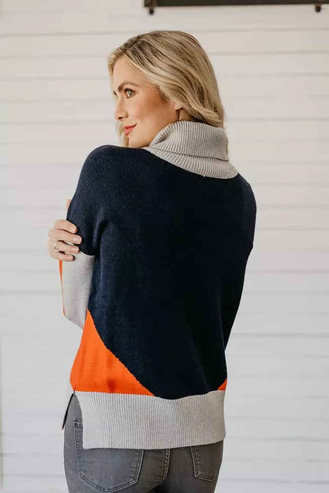 Color-block turtleneck sweater from side, dark navy with orange accent and light gray ribbed hem