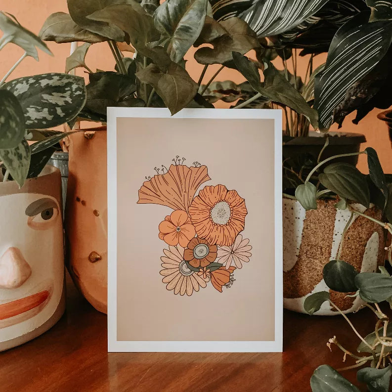 Framed floral wall art print with orange flowers surrounded by large potted plants