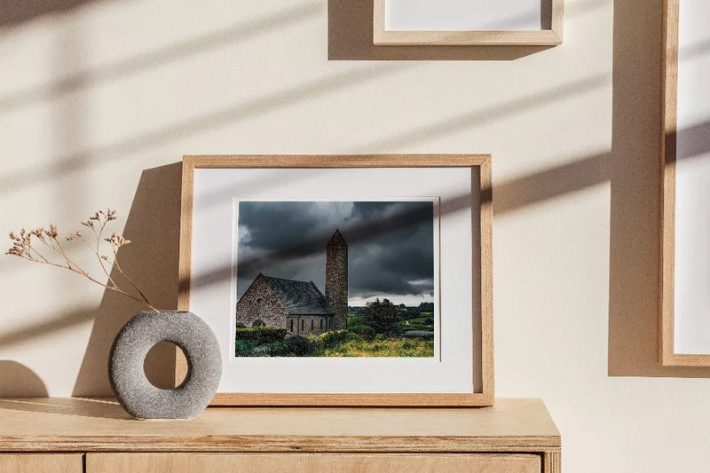 Framed landscape print showing stone church with tall tower and greenery