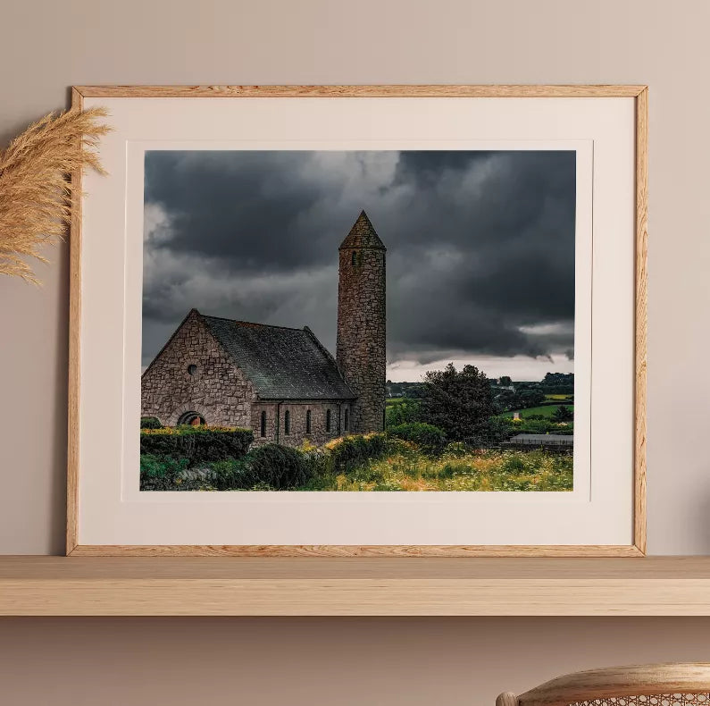 Framed landscape print of stone church tower with grassy foreground and cloudy sky