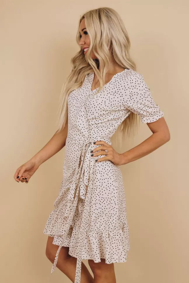 White dotted wrap dress with V-neck, short sleeves, and tie waist; flared tiered hem