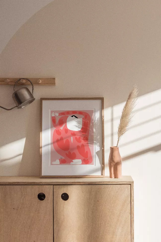 Framed wall art on shelf: red camouflage pattern with white cat, brown frame