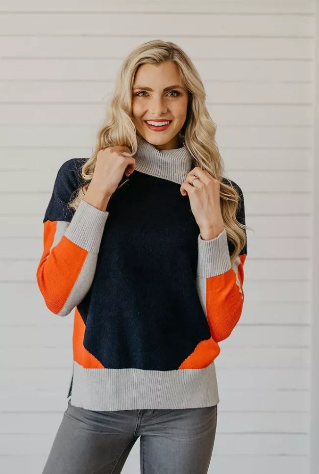 Color-block turtleneck sweater front view, dark navy body, orange sleeves, gray ribbed hem