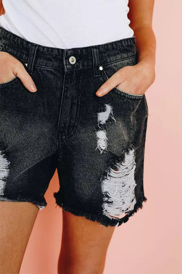 Black denim shorts close-up: button waist, distressed ripped panels, frayed edges