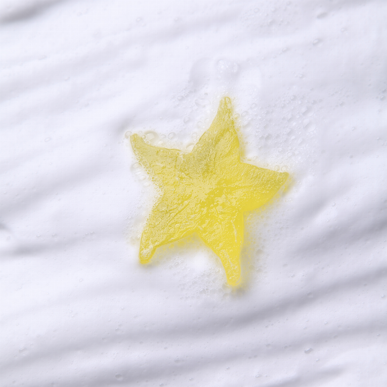 Star-shaped body soap bar in yellow on a white, bubbly surface.