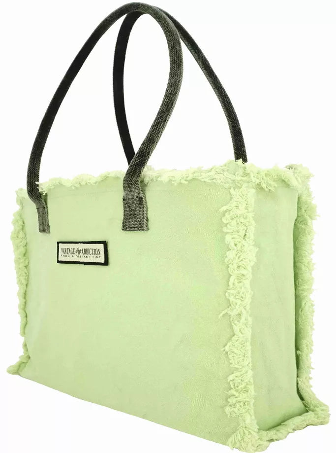 Light green tote with black handles, fringe trim, and a small front label.