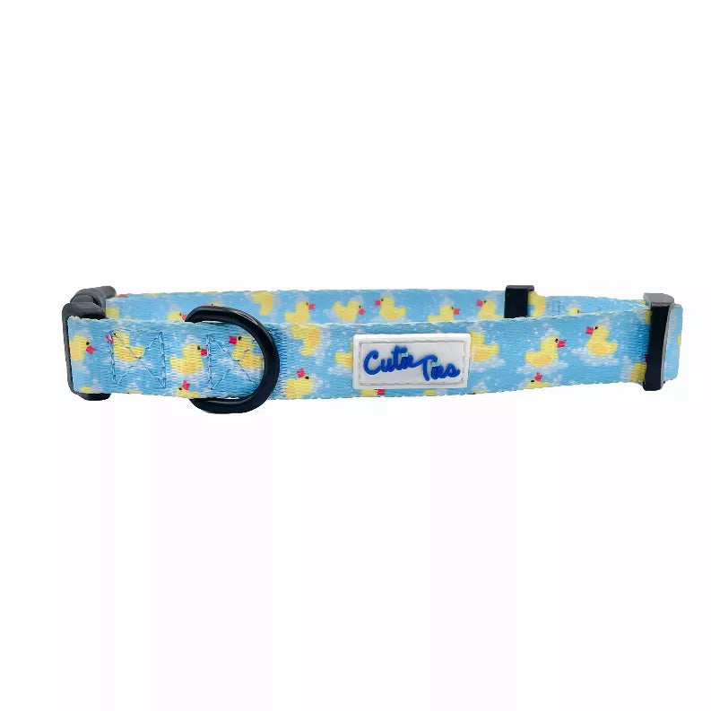 Blue fabric dog collar with duck pattern, black buckle, and stitched logo patch.