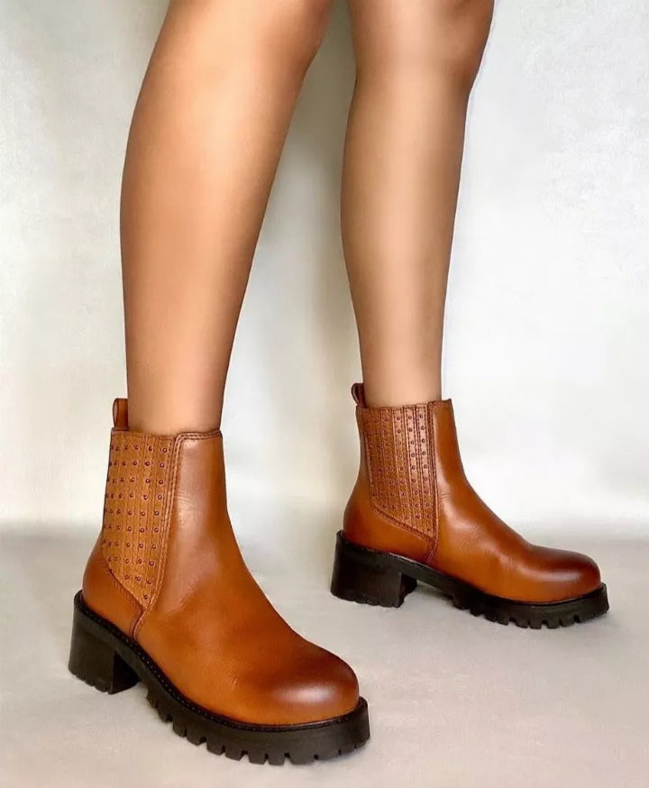 Tan chelsea boots on model legs with studded elastic panels and black lug soles.