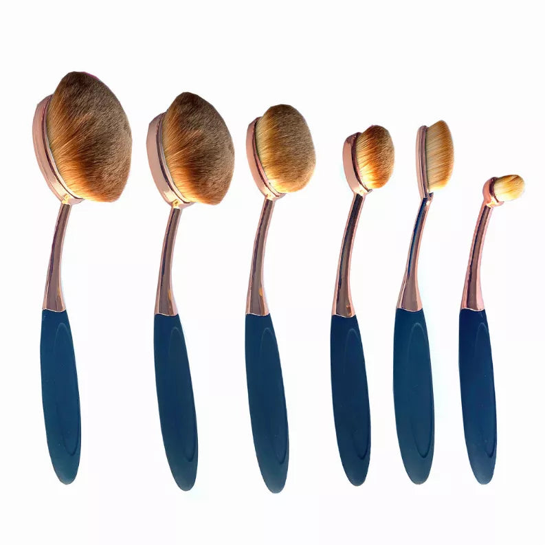 Six oval makeup brushes with copper handles and blue grips