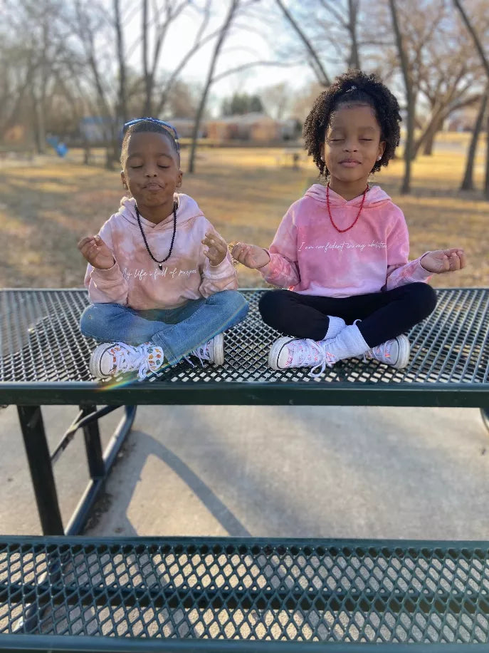 Pair of light pink plant-dyed hoodies with script affirmation, kids seated