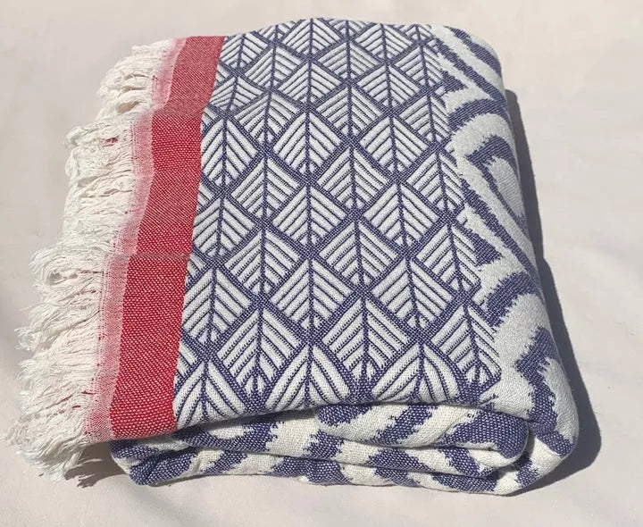Folded Turkish throw blanket with navy-and-white geometric pattern, red stripe, fringe