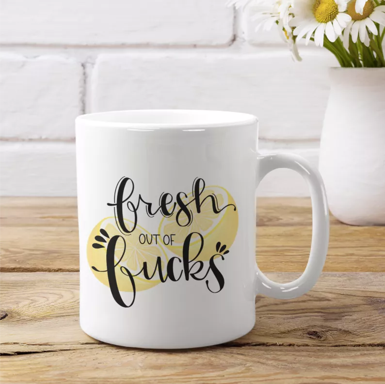 White coffee mug with 'Fresh out of Fucks' lettering and yellow heart graphic, front