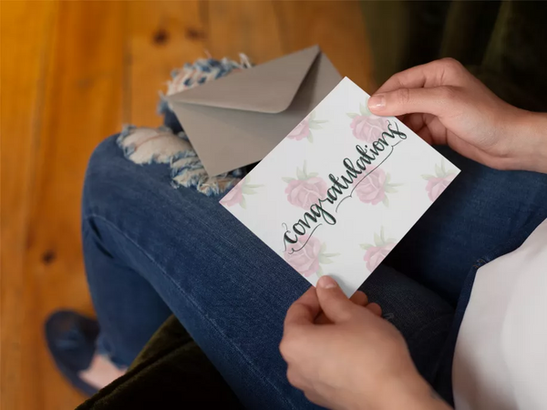Hand offering floral congratulations card with pink rose design and envelope