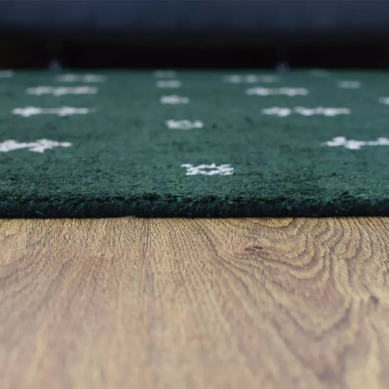 Green rug close-up showing plush pile, white motifs, and border seam