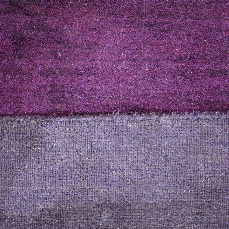 Rug pile and border close-up with purple top and gray woven backing beneath
