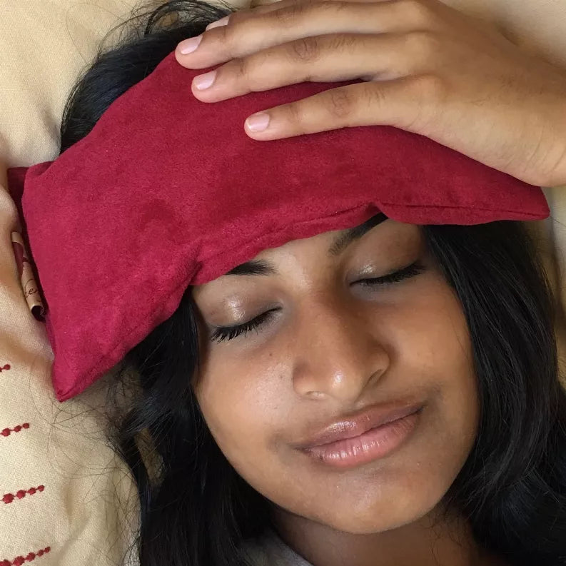 Red fabric eye pillow covering eyes, rectangular cushion with stitched border and tag.