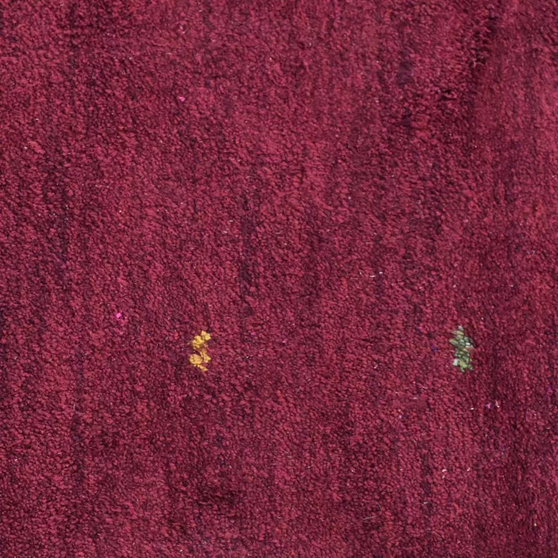 Maroon rug pile close-up with small yellow and green speckles
