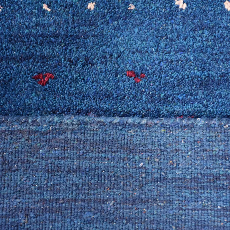 Blue rug close-up with textured loop pile and scattered red, white, and green motifs