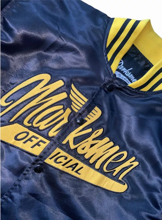Close-up of blue satin bomber jacket with yellow script graphic and striped ribbed collar