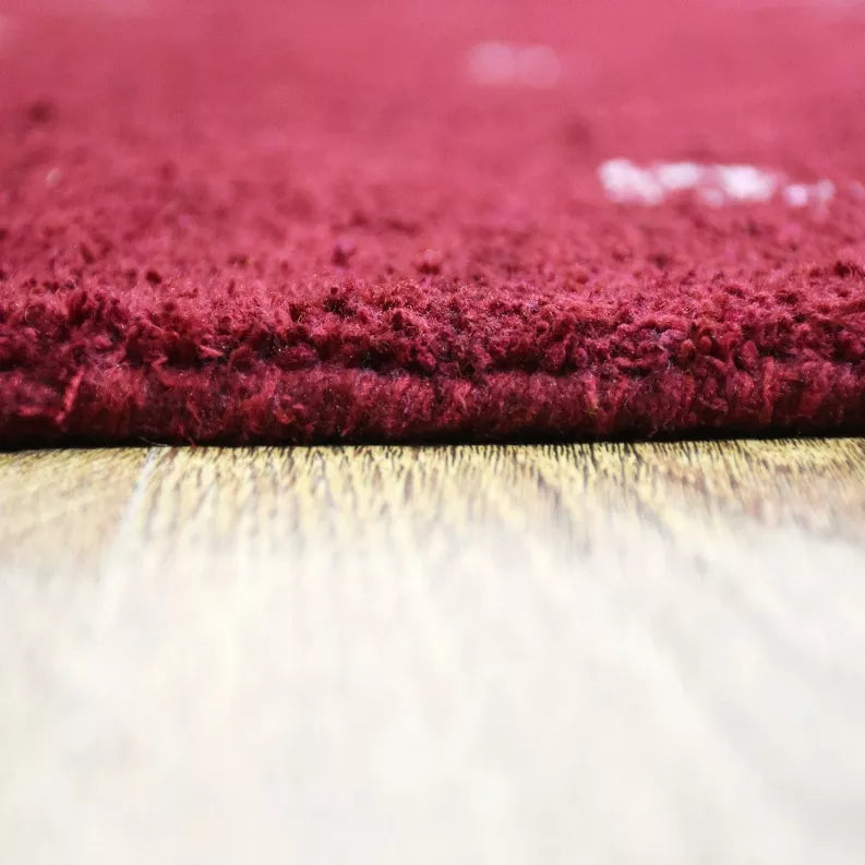 Red rug pile close-up with dark fringe and light backing along the stitched edge