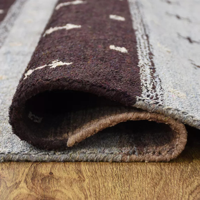 Rolled rug corner detail with textured pile and underside lining in tan and dark gray.