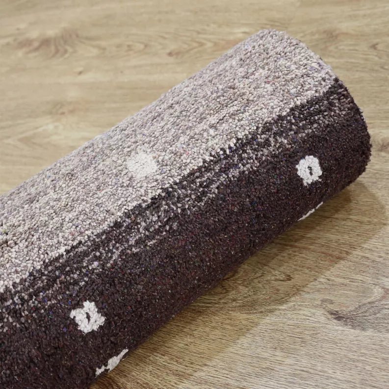 Rolled area rug corner view with light gray stripe and dark brown field plus cream icons.