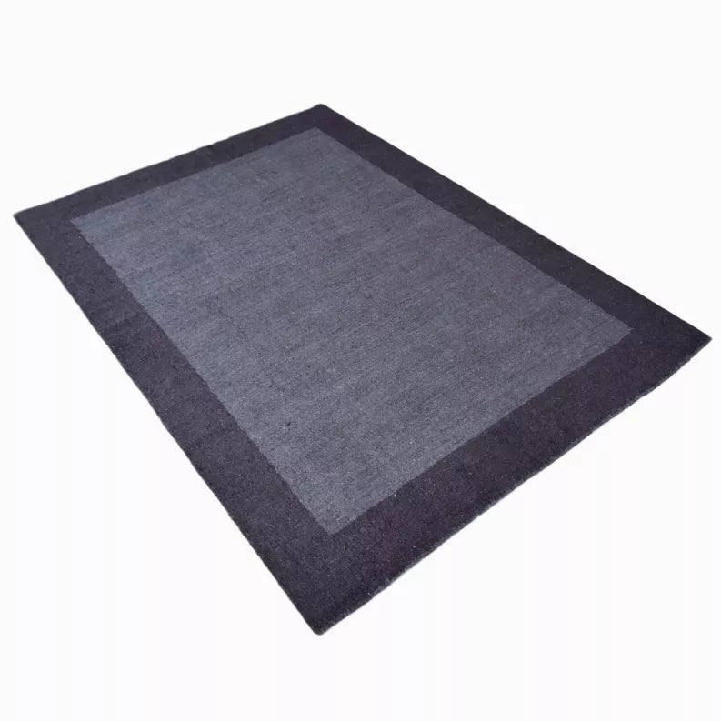 Navy-gray area rug with darker border and lighter center panel, angled view
