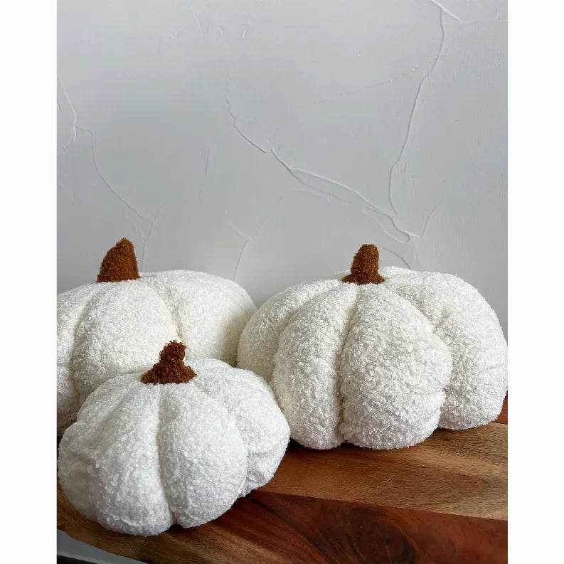 White boucle pumpkin-shaped throw pillows with brown stems on a wooden surface
