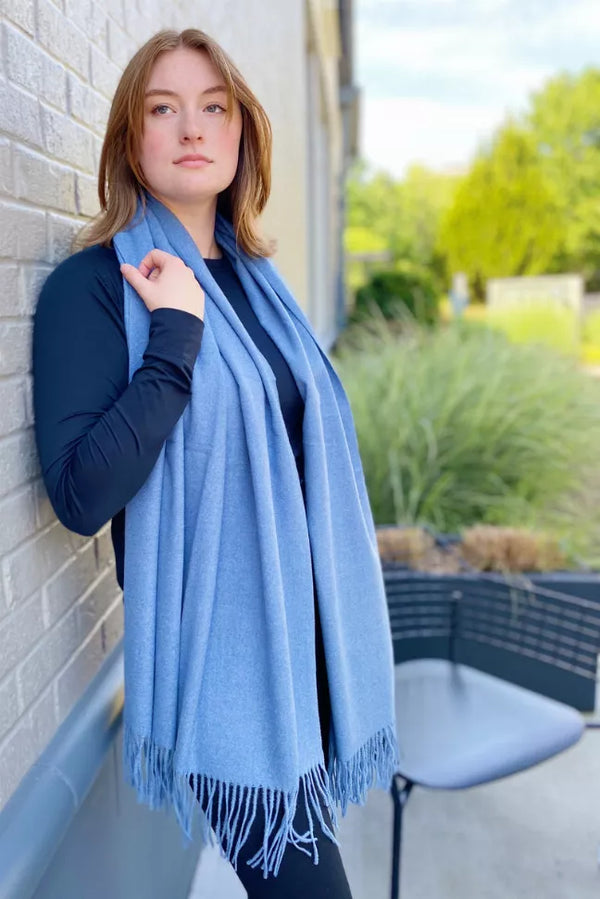Light blue cashmere-blend scarf with fringed border, held at collar
