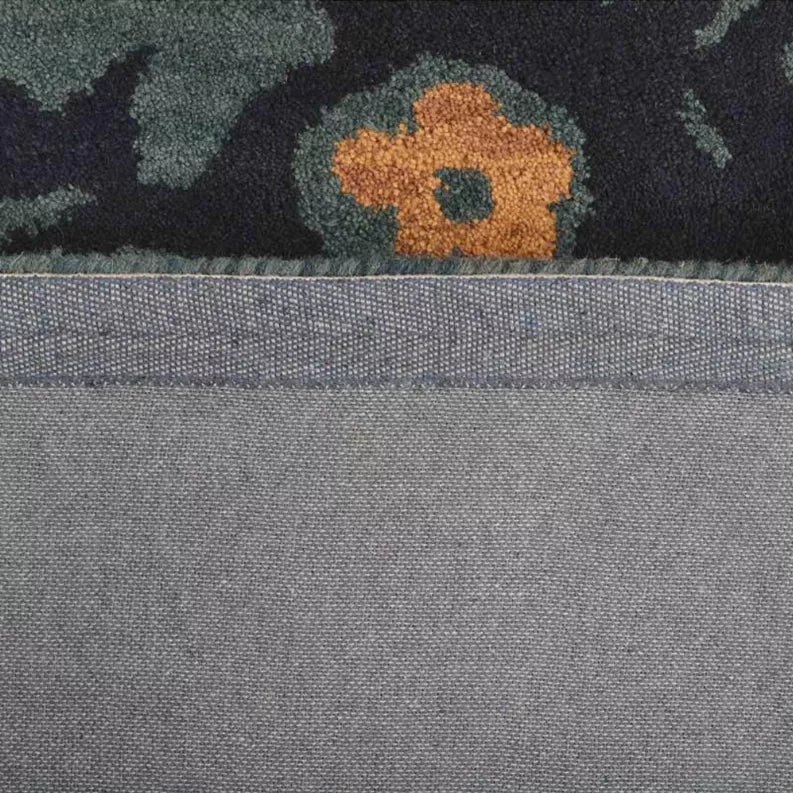 Hand-tufted wool area rug edge detail, gray backing with orange floral accent above