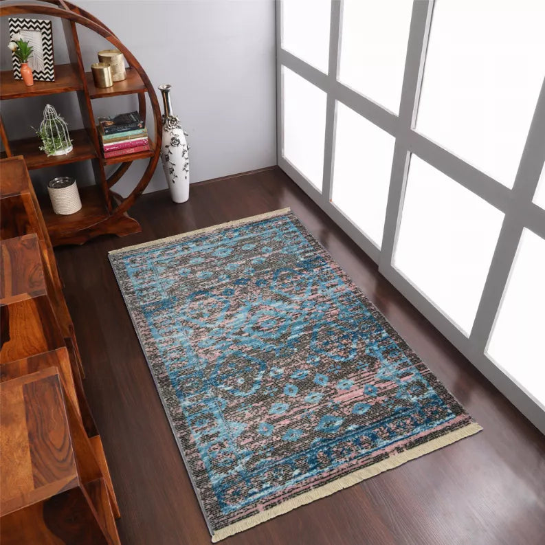 Blue geometric area rug with pink accents, border details, and short fringe on floor.
