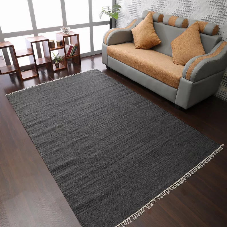 Dark gray wool kilim area rug with cream fringe border in a living room setting