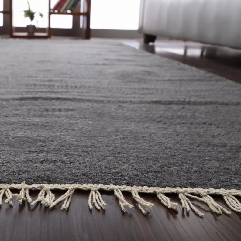 Dark gray wool kilim area rug corner with beige tassel fringe detail