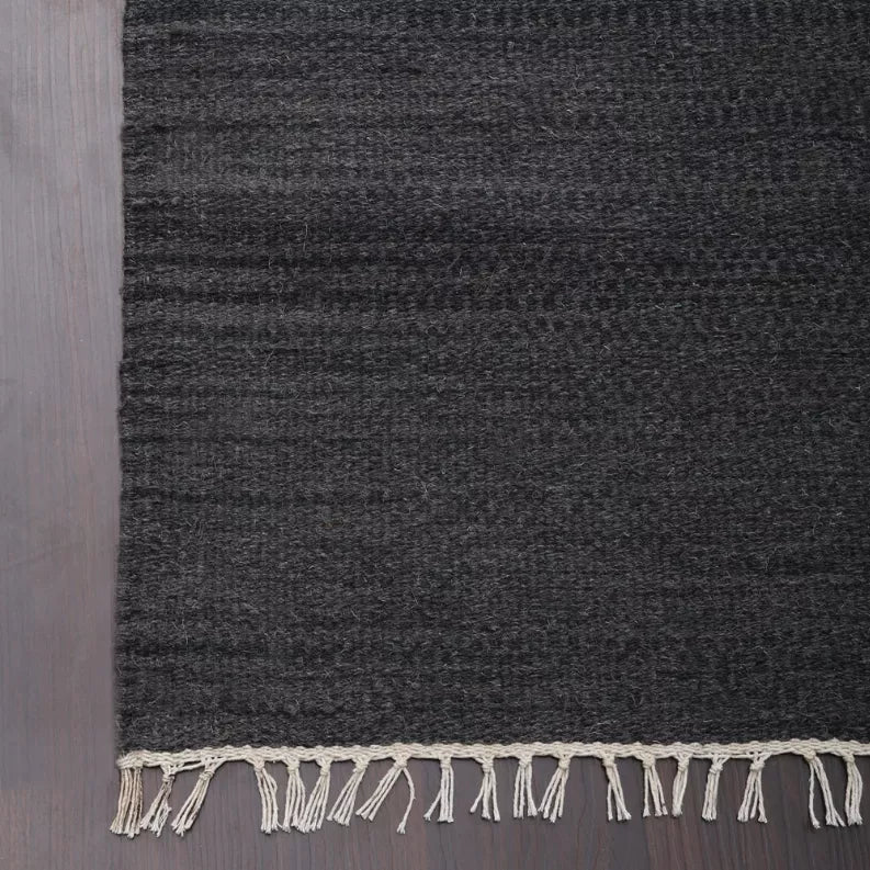Dark gray wool rug with cream fringe along the lower edge on a flat weave