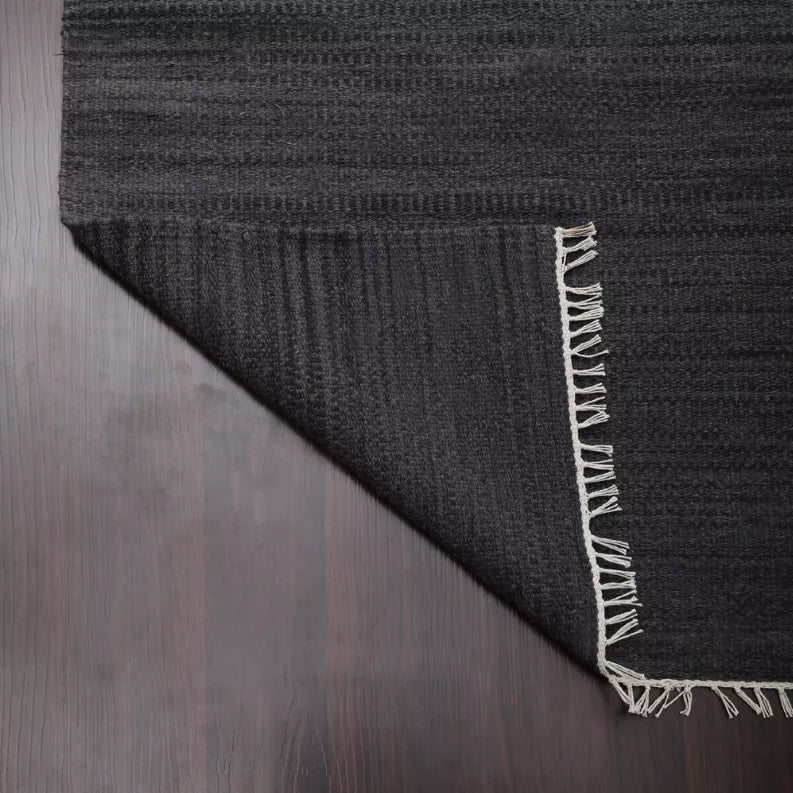 Dark gray wool kilim rug corner with light fringe and flat woven texture