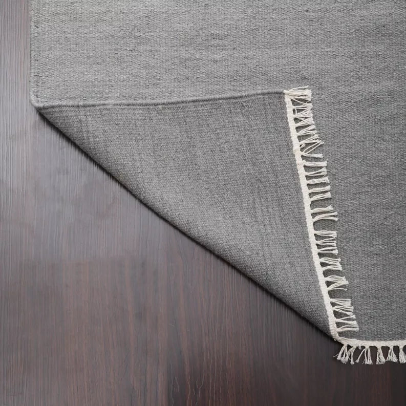 Gray flatweave wool area rug with cream fringe along edge, folded corner view