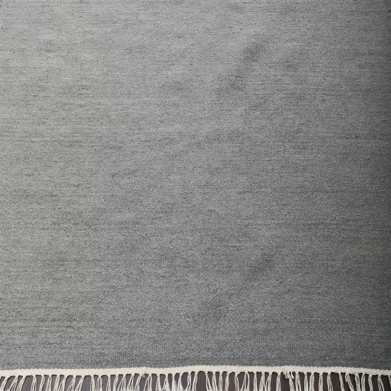 Gray rug surface with cream fringe trim along bottom edge, close-up