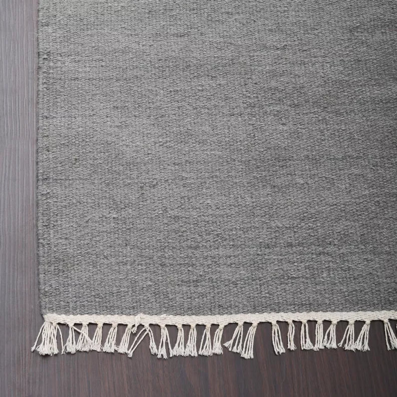 Gray rug corner with cream fringe border, close-up of edge and binding